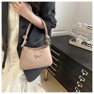 Detail of beige shoulder bag with gold bow clasp and stylish knotted handle design