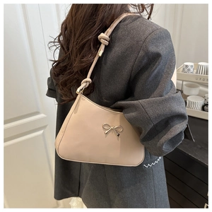 Detailed shot of beige crescent shoulder bag with metallic bow and knotted strap