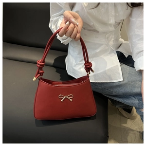 Close-up of a red leather underarm bag featuring a golden bow and twist-knot handle