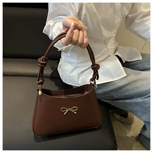 Detailed view of dark brown handbag featuring a golden bow buckle and knotted shoulder strap