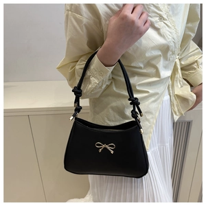 Detail of a black leather underarm bag featuring a golden bow and knotted strap design