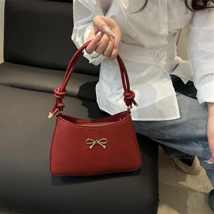 Dark red matte leather shoulder bag with gold bow and unique knotted handles shown by model
