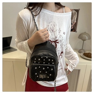 Close-up of black quilted mini backpack with silver rivets and metal chain straps