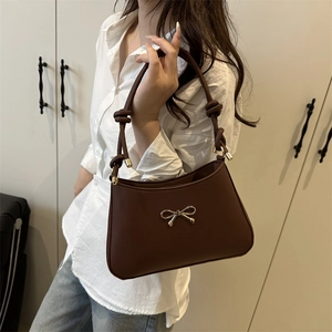 Brown leather shoulder bag with gold bow ornament and unique knotted strap detail