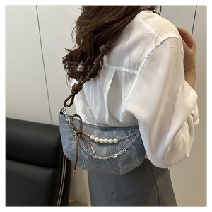 Détail du sac demi-lune en denim bleu clair avec perles décoratives et chaînes en métal