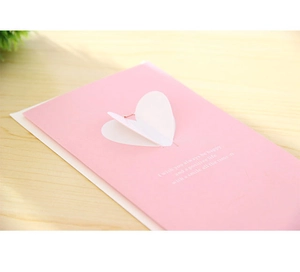 Gros plan d'une carte de vœux 3D rose avec cœur ailé et enveloppe sur table bois