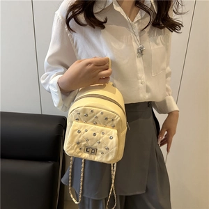Mini quilted light yellow backpack with silver studs and chain strap shown by a model