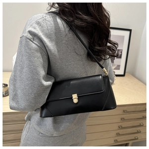 Side view of black baguette bag with gold buckle on shoulder of model in grey suit