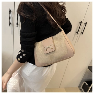 Detail of beige shoulder bag featuring a gold bow clasp and shimmering matte texture