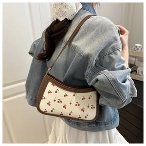 Detail of a chic baguette bag with cherry prints and brown leather trim on a denim jacket