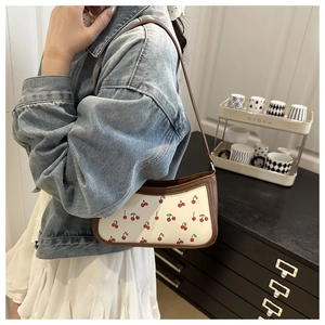 Detail of vintage white shoulder bag with red cherry pattern and brown leather trim