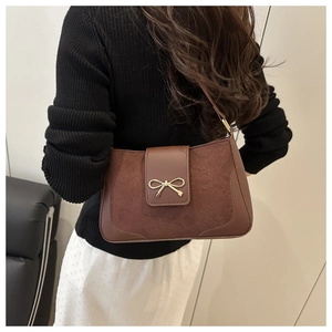 Detail of dark brown saddle bag featuring suede texture and golden bow clasp on model