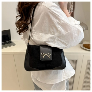 Detailed view of black baguette bag with gold bow clasp on a model in a lifestyle setting