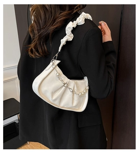 Detail of white pleated crescent bag with pearl and floral metal chain on black suit