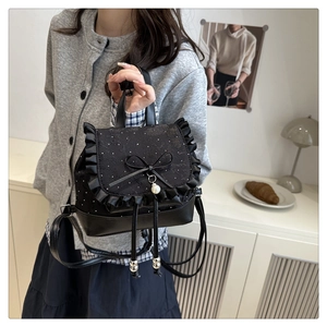 Detail of black lace backpack featuring a pearl bow charm and ruffled edge design