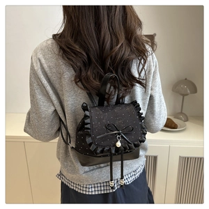 Detail of black polka dot backpack featuring ruffles, a bow, and a pearl pendant