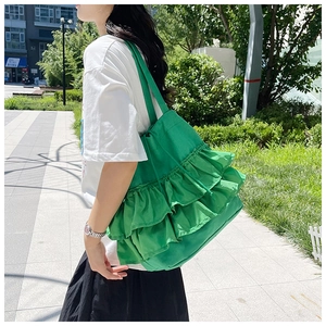 Detail of green pleated canvas tote bag featuring multi-layer ruffles on a shoulder strap