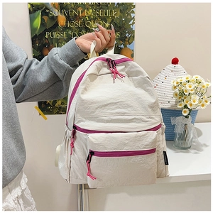 Detailopname van de gebroken witte nylon rugzak met opvallende magenta ritsen en zakken