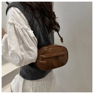 Detail of a dark brown glossy crossbody bag with adjustable strap and gold hardware