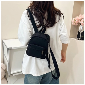 Close-up of black canvas mini backpack featuring brand logo tag and zip pockets