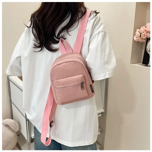 Detail view of a pink mini nylon backpack with branded side tag on a model's back
