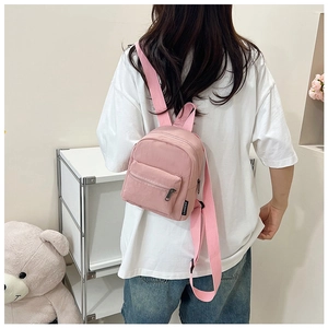 Pink mini backpack with adjustable straps shown in use against a cozy background