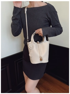 Dettaglio borsa a secchiello in pelle beige con lucchetto dorato e ciondolo a sorriso