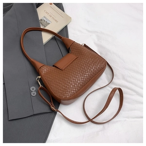 Detalle de un bolso hobo marrón de textura trenzada con bandolera sobre una chaqueta gris