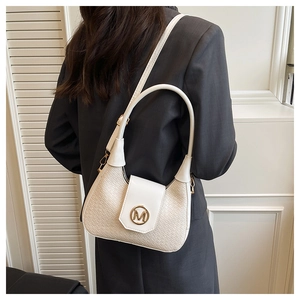 Detalle del bolso media luna crema con textura tejida y hebilla dorada en forma de M