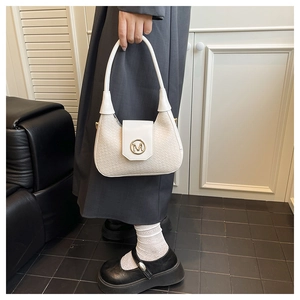 Detalle de bolso de hombro trenzado crema con logo M dorado mostrado en una modelo