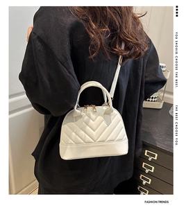Detailed view of cream shell bag featuring V-shaped quilting and gold metal zippers