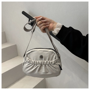 Close-up of beige nylon pleated bag featuring a metallic M logo and adjustable strap