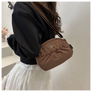 Brown ruched crossbody bag with silver M logo and wide strap worn by a model