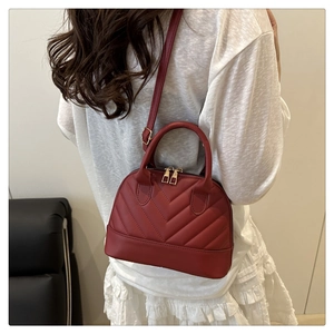 Model wearing a burgundy shell bag with V-shaped quilting and gold metal top handles