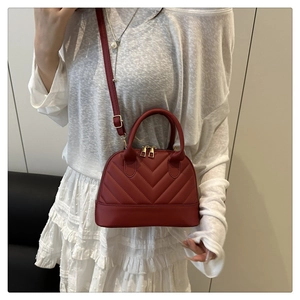 Detail of burgundy shell bag featuring elegant V-shaped quilting and gold zippers