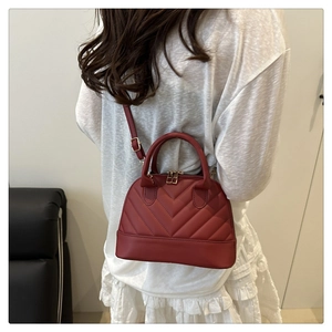 Rear view of wine red quilted shell bag worn crossbody over a white lace dress