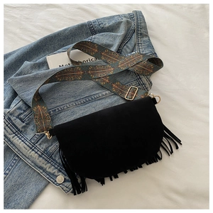 Detail of black suede saddle bag with ethnic pattern wide strap and long fringe tassels