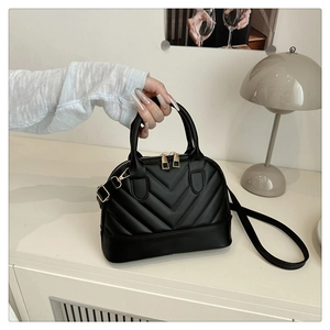 Detail of black V-quilted shell handbag with gold hardware on a stylish indoor table