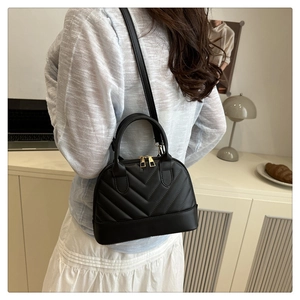 Detail of a black quilted shell bag with gold hardware worn as a crossbody purse