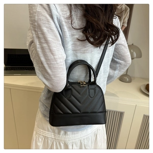Detail of a black V-quilted mini shell bag with dual handles and crossbody strap
