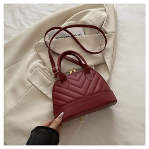 Detail of burgundy shell bag with V-shaped quilting, dual handles, and golden hardware