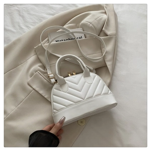 Detail of white quilted shell bag with gold hardware and V-shaped stitching pattern