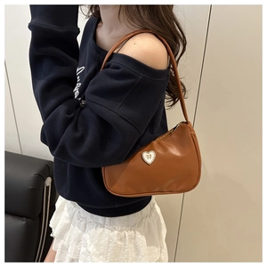 Detail of warm brown crescent hobo bag with heart metal emblem worn on the shoulder