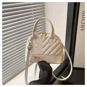 Detail of white V-quilted shell bag featuring gold zippers and circular top handles