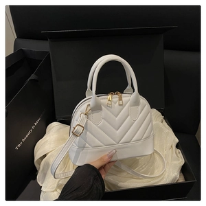 Detail of white shell bag with V-quilted stitching and gold hardware in a gift box