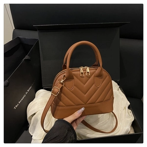 Close-up of caramel V-quilted shell bag on luxury gift box with golden hardware details