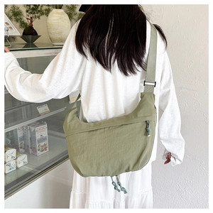 Model wearing a light green nylon dumpling bag with adjustable strap in minimalist cafe