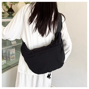 Detailed back view of a large black nylon crossbody crescent bag on a model in a cafe