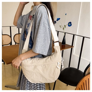 Side view of a beige crescent crossbody bag in soft wrinkled nylon with a wide strap