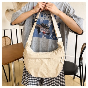 Detail of a beige nylon crescent bag featuring adjustable straps and side drawstring accents